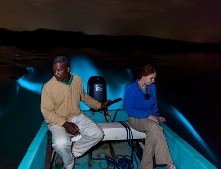 Clifford steers the boat through the bioluminescent lagoon as Kelci is awestruck by the brilliant blue glow of the boat wake 